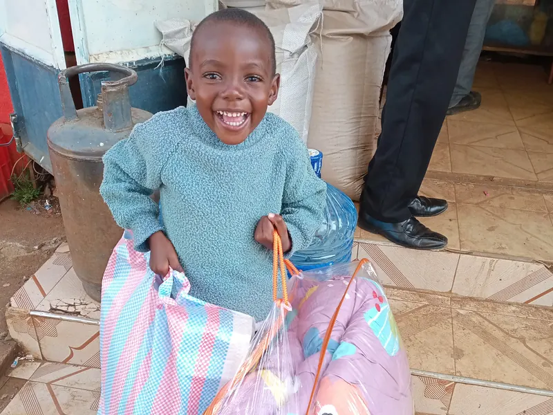 A smiling child holds two bags of new blankets