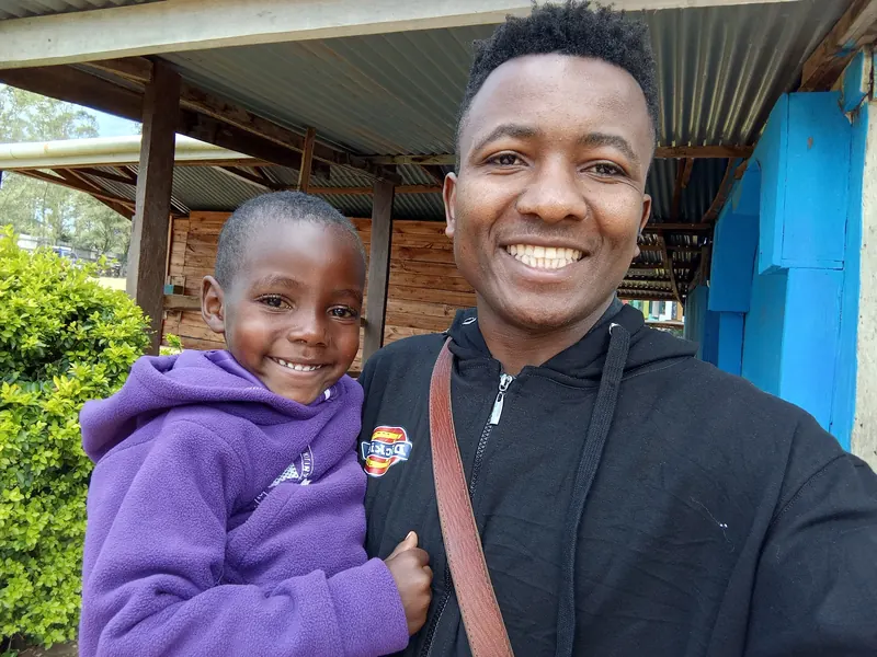 A young man takes a selfie with a smiling child in a purple jacket