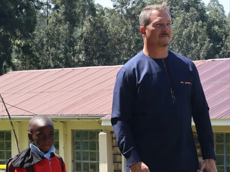 A man stands beside a boy in a red jacket outside a school building
