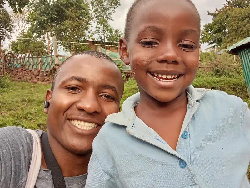 A young man takes a smiling selfie with a boy outdoors