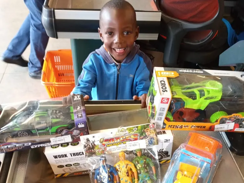 A smiling boy behind a counter covered in new toys